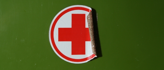 in sich teilweise ablösender Aufklber mit Rotem Kreuz vor grünem Untergrund