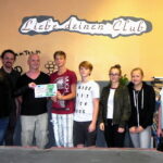 Landtagsabgeordnete Janina Pfau, Kreisvorstandsmitglied Maik Schwarz und Stadträtin Helga Meyer übergeben einen Scheck (150,- €) an Maik Friedrich und die Besucher des Jugendtreffs Lengenfeld. Im Hintergrund eine orange Wand, darauf der Spruch "Liebe deinen Club"